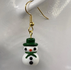 white lampwork snowman earring with green hat and scarf hanging from mannikin's earlobe