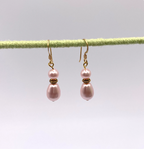 Pair of pink pearl earrings on a thin green rod against a light gray background