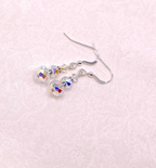 A pair of sterling silver dangle earrings with faceted clear crystal beads, displayed on a textured light pink background.