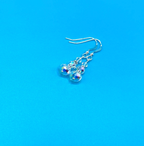 A pair of sterling silver dangle earrings with faceted clear crystal beads, photographed on a solid bright blue background.