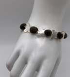 A beaded bracelet displayed on a white mannequin hand. The bracelet features grayish brown velvety mgambo beads alternating with translucent white mother-of-pearl butterfly-shaped beads.