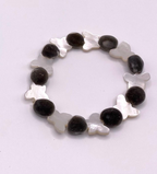 A beaded stretch bracelet featuring alternating fuzzy grayish brown oval mgambo beads and white mother-of-pearl butterfly-shaped beads, displayed on a light off-white background.
