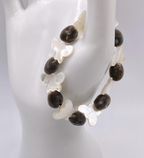 A beaded stretch bracelet displayed on a white mannequin hand. The bracelet features grayish brown mgambo seed beads and white mother-of-pearl butterfly-shaped beads.