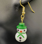 white lampwork snowman earring with green hat and scarf hanging from black mannikin earlobe