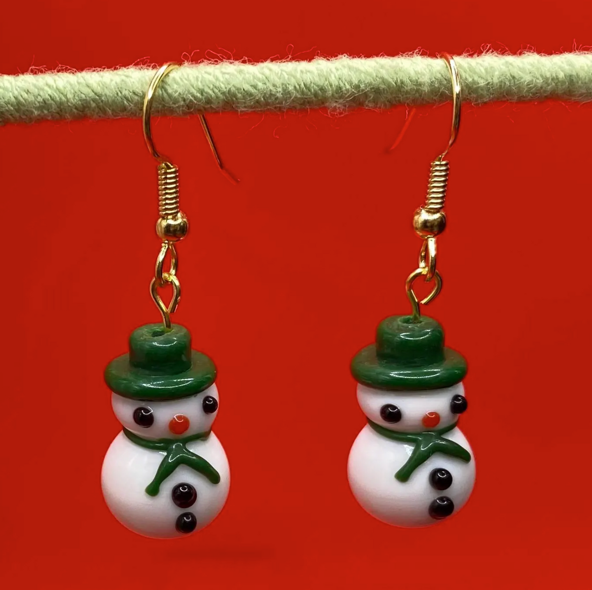 white lampwork snowmen earrings with green hat and scarf hanging from green rod