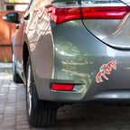Car's rear end with a red and blue crab sticker on a brick road.