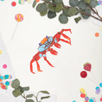Colorful red and blue crab sticker on a white background with green leaves and colorful candies.