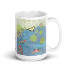 A white ceramic mug featuring a colorful printed illustration of a pond scene with a yellow-and-black butterfly, green lily pads, red flowers, a large frog, and small frogs on a log, shown on a clean white background.